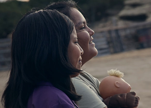 Two young girls smile while looking off into the distance. One of them holds a doll. 
