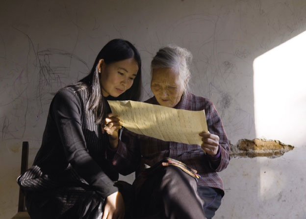A young woman and an old woman look intently at a large piece of yellowed paper. 