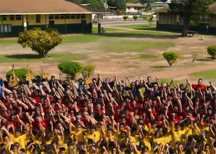 Large group of people in white, red, or white shirts singing and dancing in unison, arms in the arm.