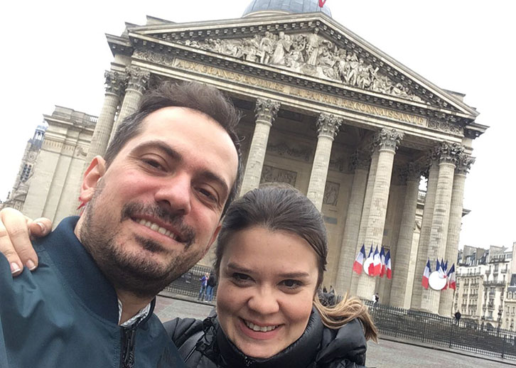 Selfie of two people embraced in front of grand Neoclassical marble building with columns.