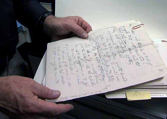 Closeup on a pair of hands holding up a page of handwritten notes from a manila folder.