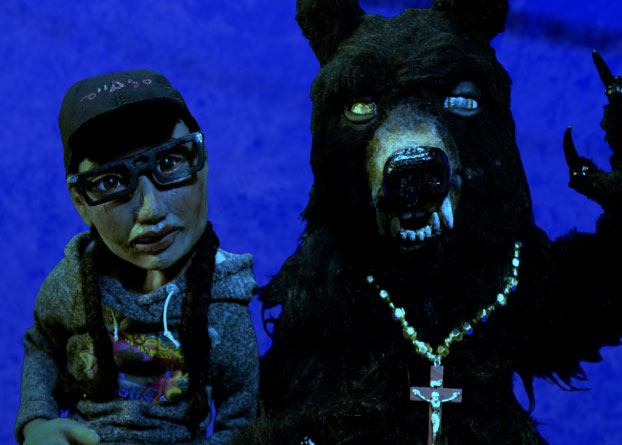 A stop-motion animation frame with a clay human figure and bear sit side by side. 