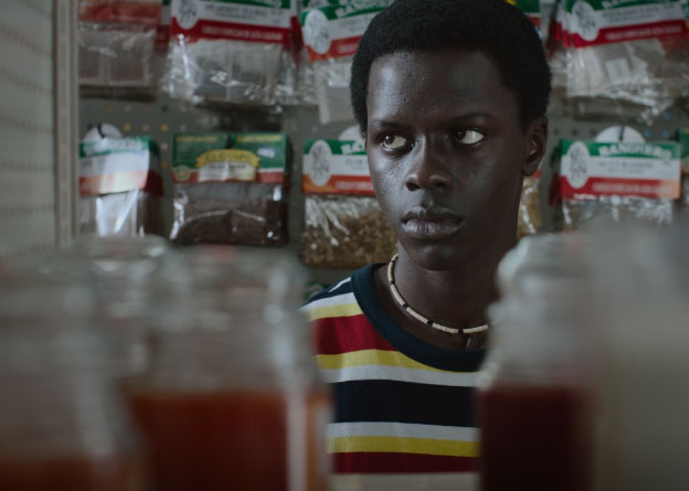 A teenager in a store glances out of frame; behind him are bags of spices. 